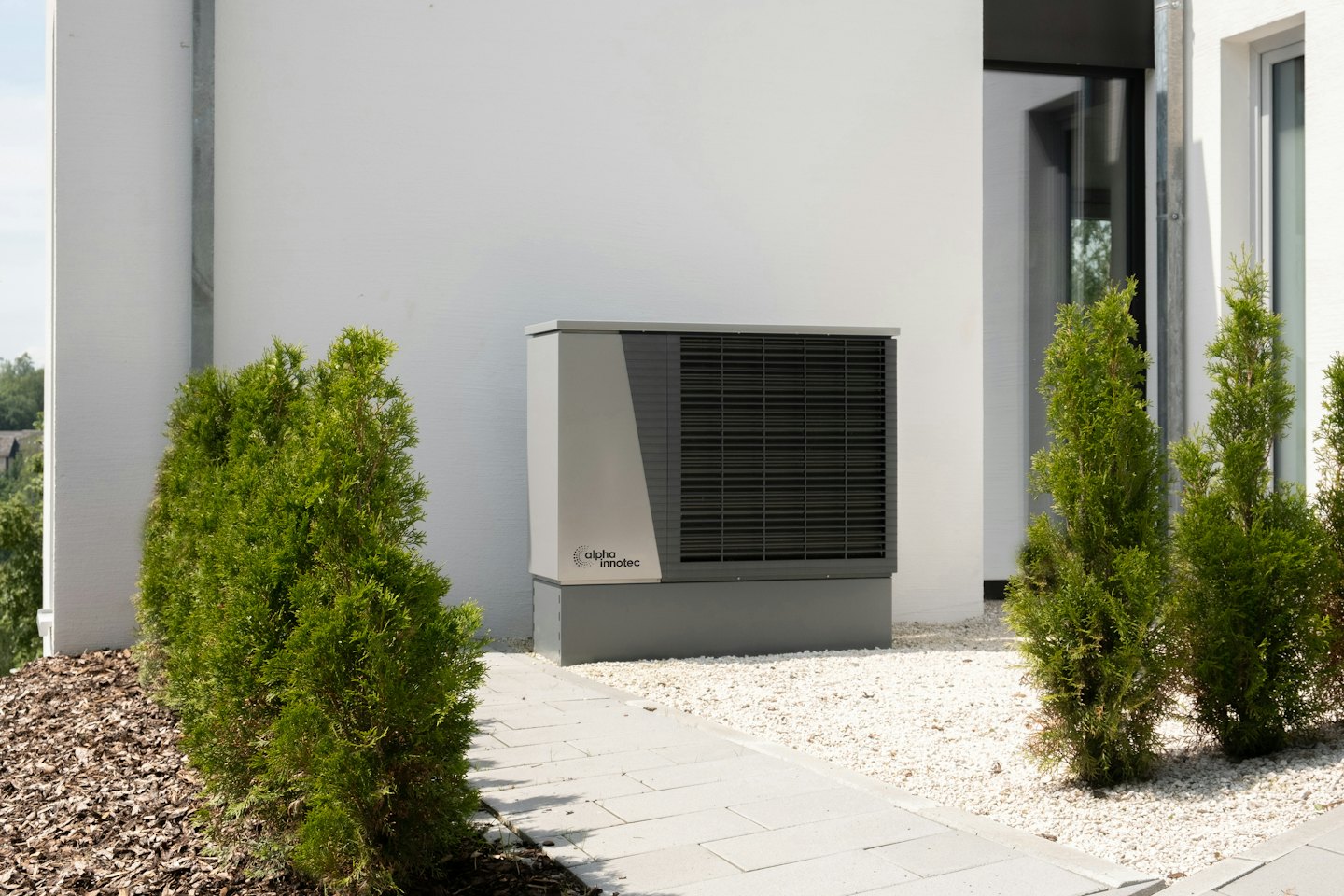 Unità esterna di una pompa di calore accanto a un edificio bianco in una giornata di sole.